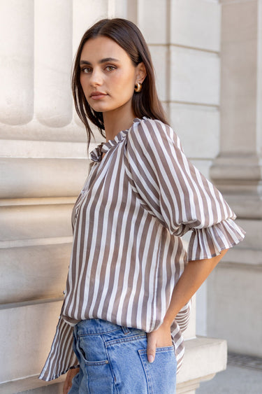 Woman in a striped shirt and jeans standing against classical architecture.
