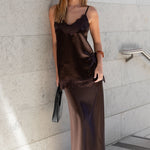 Woman in a brown satin dress standing against a light gray wall.