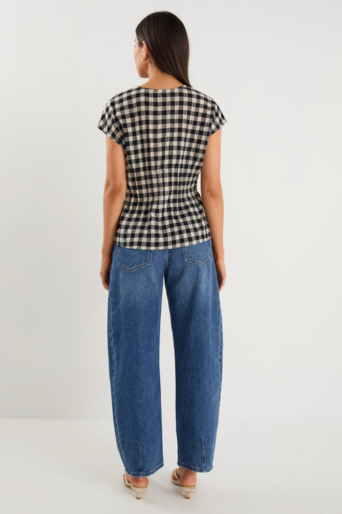 Woman wearing a sleeveless black and ecru gingham vest with tie-front detailing, styled with dark blue jeans and neutral flats.