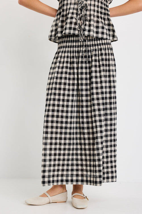 Woman wearing a black gingham maxi skirt with shirred waist, tiered design, and side split, styled with light flat shoes.
col_pattern