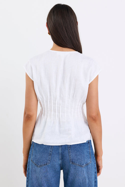 Woman wearing an ivory linen cap sleeve vest top with tie-up front detail, paired with blue denim jeans, standing against a white background.
