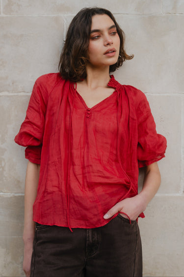 Woman wearing a red blouse against a beige wall
