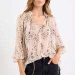 Woman wearing a beige floral blouse and black pants on a white background