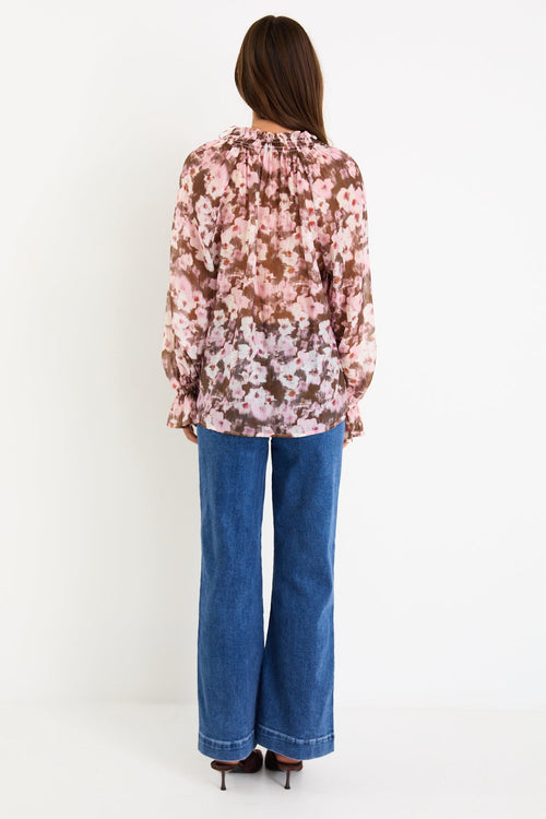 Model wearing a blush and chocolate floral long sleeve top with a shirred neckline and floaty silhouette