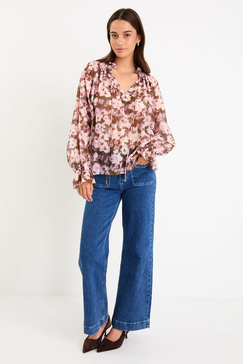 Model wearing a blush and chocolate floral long sleeve top with a shirred neckline and floaty silhouette