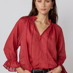 Woman wearing a red blouse and blue jeans against a plain background