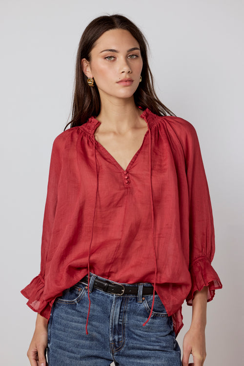 Woman wearing a red blouse and blue jeans against a plain background
