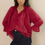 Woman wearing a red blouse with puffed sleeves against a beige background