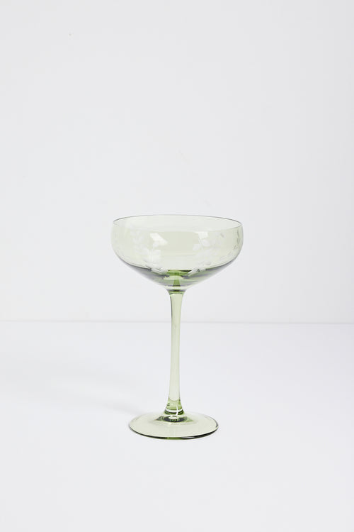 A single light green champagne coupe glass with a wide, shallow bowl, a slender stem, and a flat circular base, photographed against a seamless white studio background.