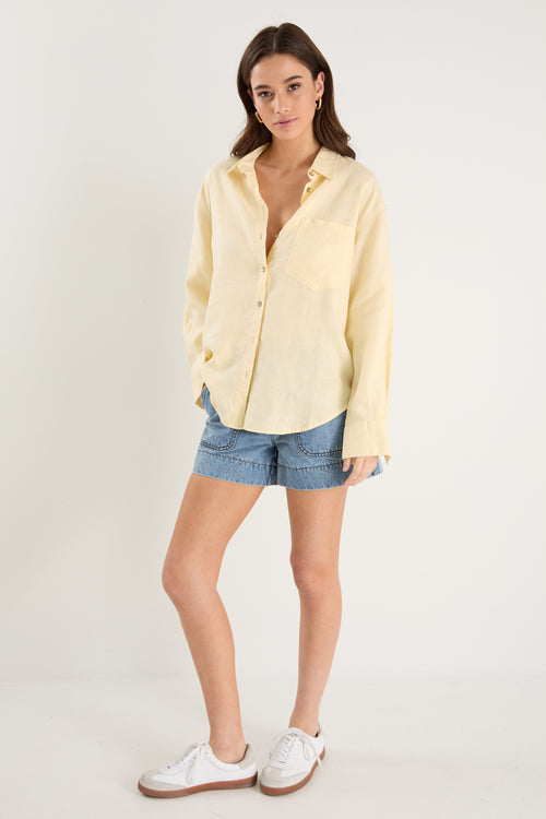 Model wears a yellow linen shirt with denim shorts and white sneakers