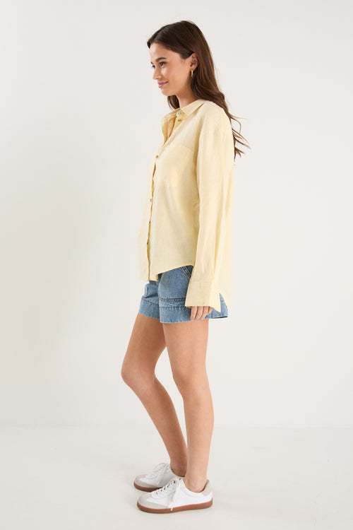 Model wears a yellow linen shirt with denim shorts and white sneakers