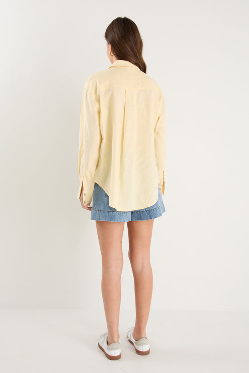 Model wears a yellow linen shirt with denim shorts and white sneakers