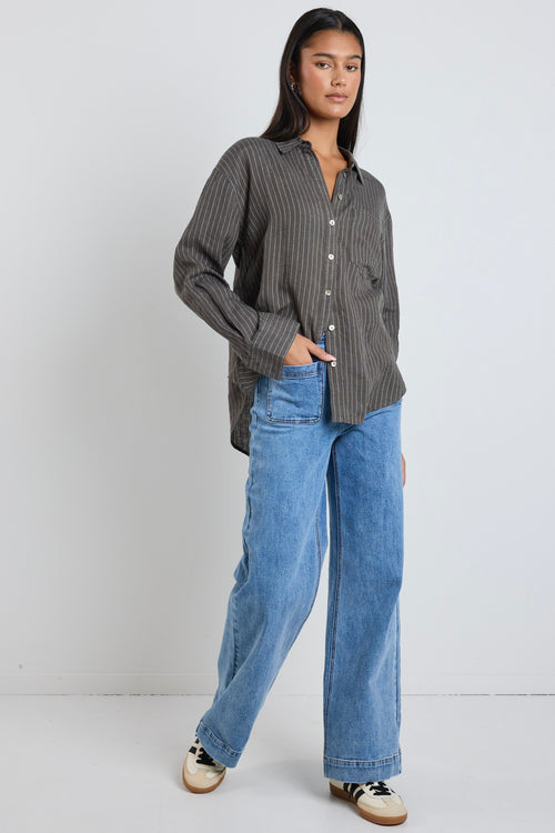 model wears a khaki stripe button up collared shirt with blue jeans