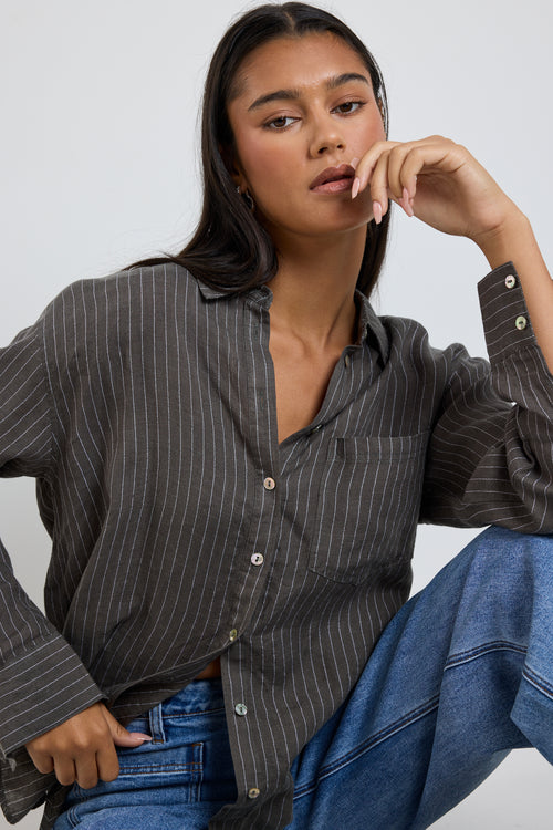 model wears a khaki stripe button up collared shirt with blue jeans