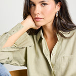 Model wears a moss green linen button up collared shirt with light blue jeans