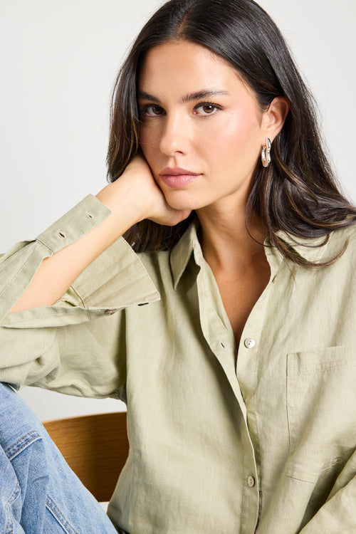 Model wears a moss green linen button up collared shirt with light blue jeans