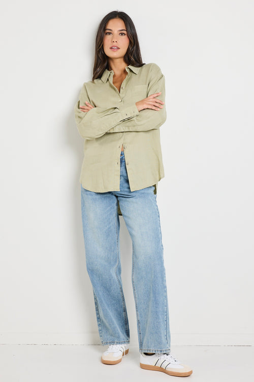 Model wears a moss green linen button up collared shirt with light blue jeans