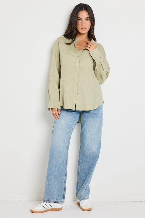 Model wears a moss green linen button up collared shirt with light blue jeans