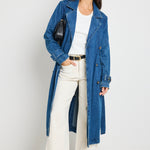 Model wears blue denim trench coat with tie waist and buttons