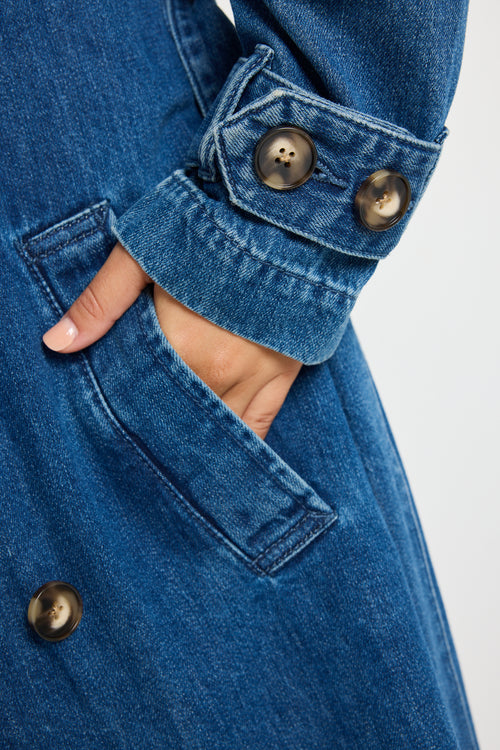 Model wears blue denim trench coat with tie waist and buttons