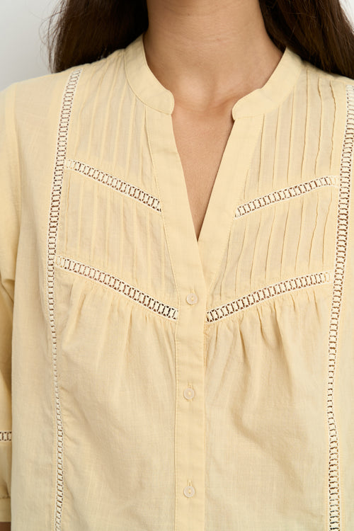 Woman wearing a soft yellow cotton blouse with pintuck and ladder lace details, styled with light blue wide-leg jeans.