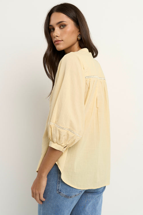 Woman wearing a soft yellow cotton blouse with pintuck and ladder lace details, styled with light blue wide-leg jeans.
