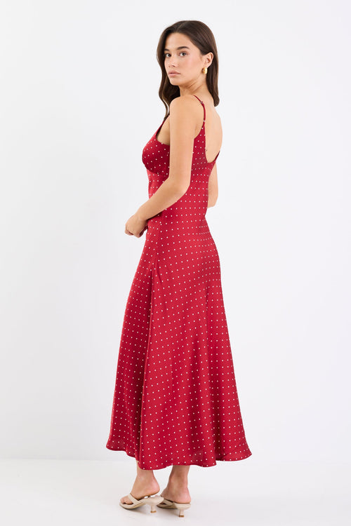 Woman wearing a red satin midi dress with white polka dots, adjustable spaghetti straps, and a bias-cut silhouette, standing against a white background.