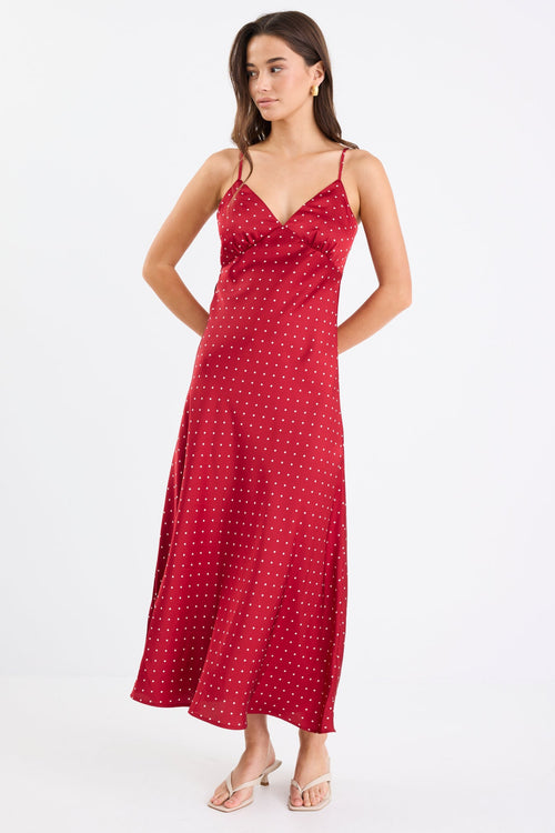 Woman wearing a red satin midi dress with white polka dots, adjustable spaghetti straps, and a bias-cut silhouette, standing against a white background.