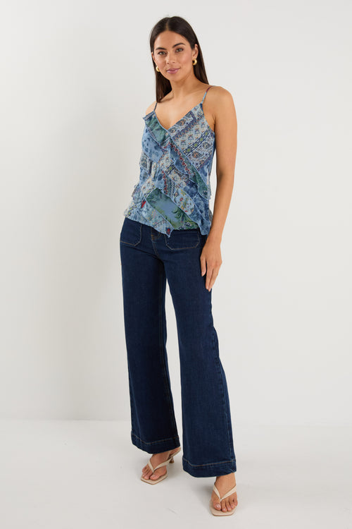 Woman wearing a strappy blue floral scarf-print top with ruffle detailing, styled with indigo jeans.