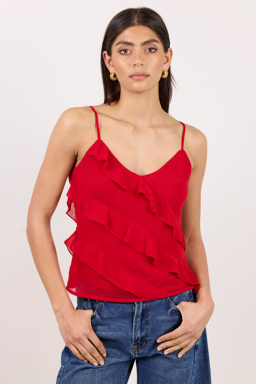 A woman modeling a red ruffled spaghetti-strap camisole top paired with blue jeans, set against a plain light background.