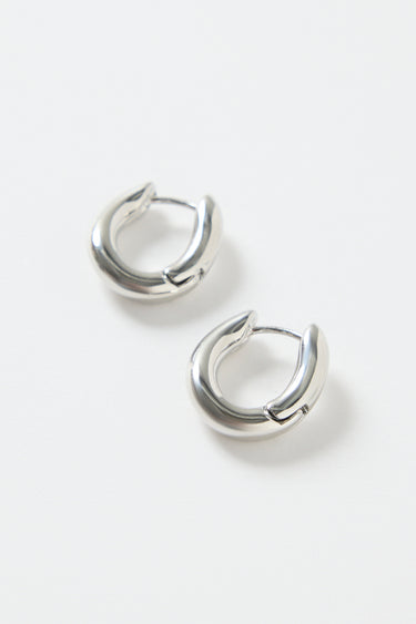 A pair of small oval-shaped wavy rhodium hoop earrings photographed on a clean white background.