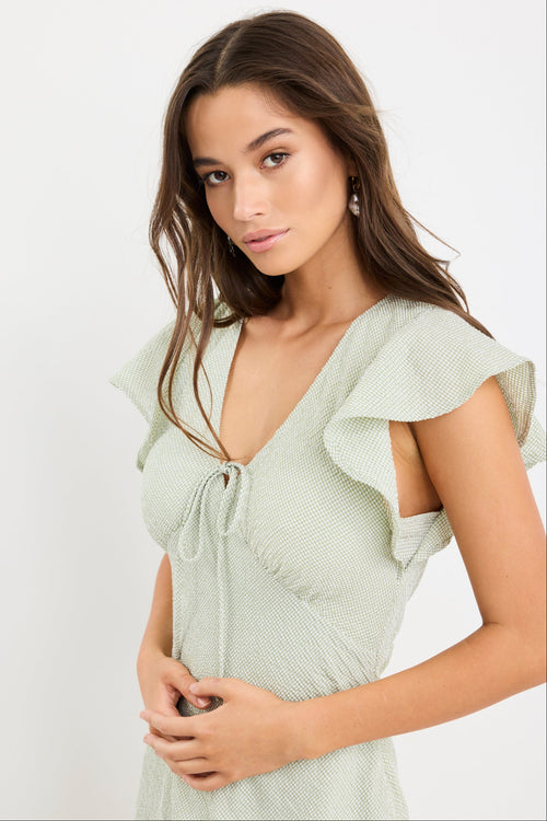 Woman wearing a sage green gingham midi dress with flutter sleeves and keyhole tie neckline.