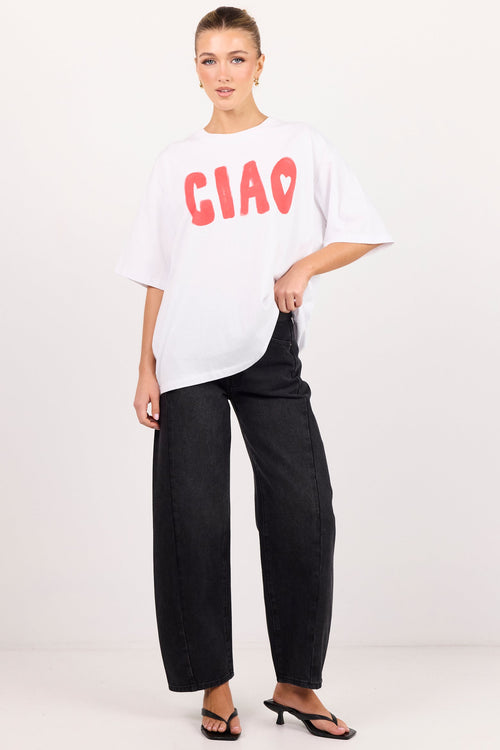 A woman modeling an oversized white t-shirt with 'CIAO' printed in red across the chest, paired with black wide-leg pants and black sandals, against a plain white studio background.