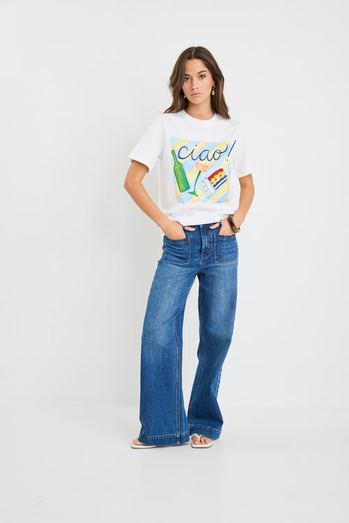 Woman wearing a white t-shirt with colorful graphics and blue jeans on a white background