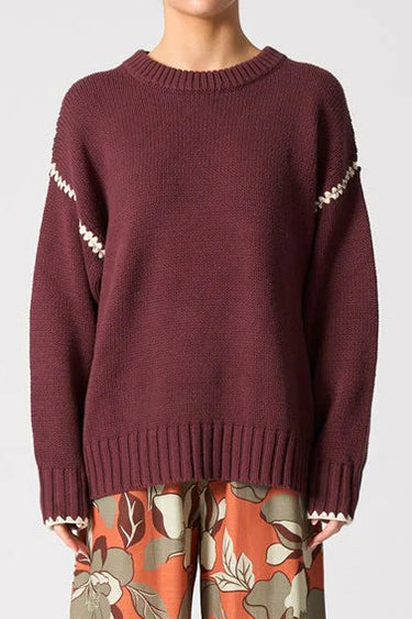 Person wearing a maroon sweater and floral-patterned pants on a white background