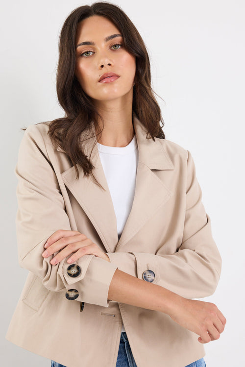 Woman wearing a beige blazer over a white shirt with a plain background
