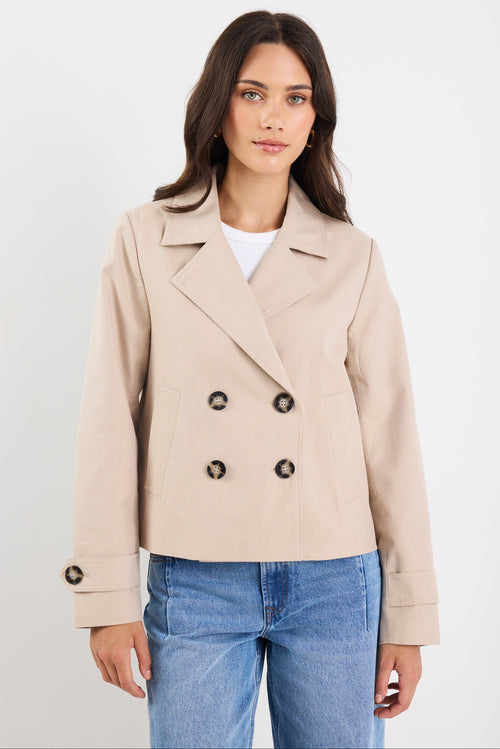 Woman wearing a beige trench coat with black buttons on a white background