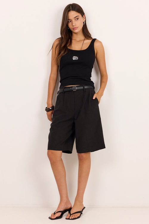 A woman modeling a black sleeveless tank top, black wide-leg shorts, a black belt, and black sandals against a plain off-white studio background.