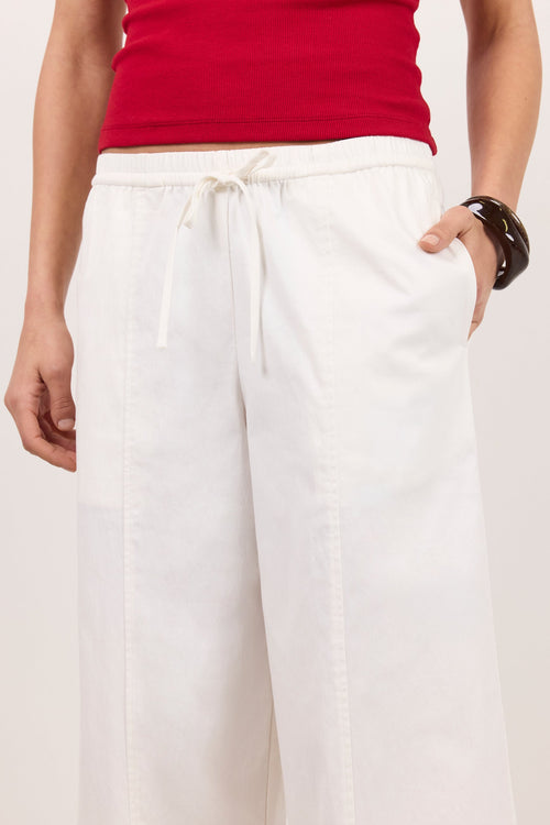 White wide-leg drawstring pants worn by a model, paired with a red top, against a light beige studio background.