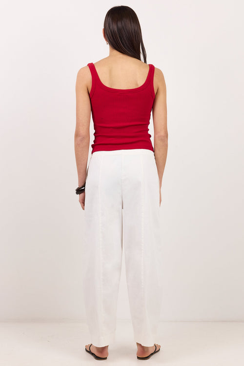 A woman viewed from behind wearing a red sleeveless tank top and white wide-leg pants, standing against a plain light background.
