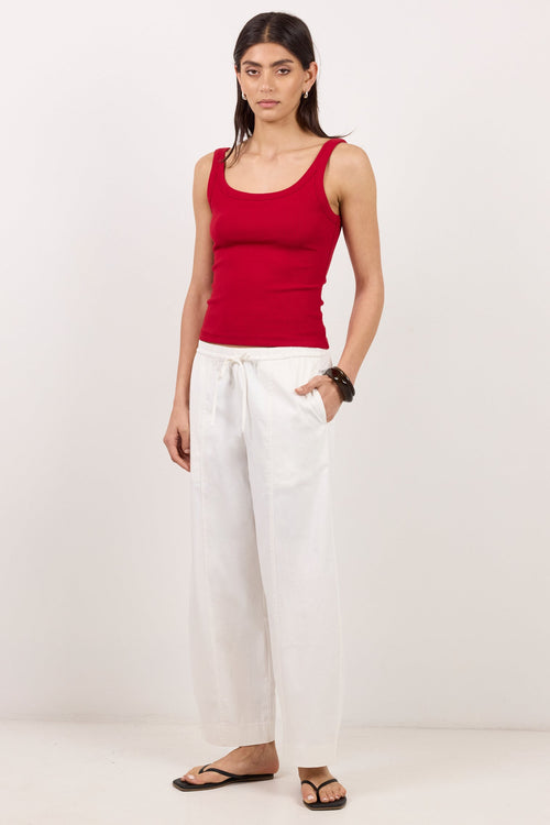 A woman modeling a red ribbed tank top and white wide-leg linen pants, standing against a plain white studio background.