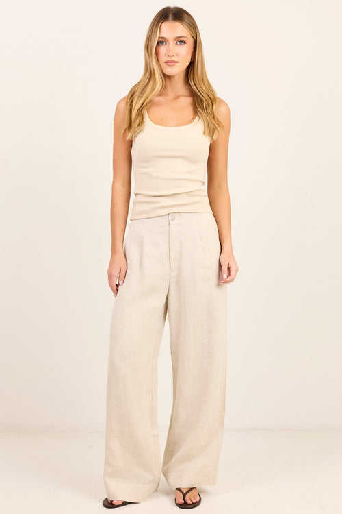 A woman modeling a light beige ribbed tank top and matching wide-leg linen pants against a clean, off-white studio background.