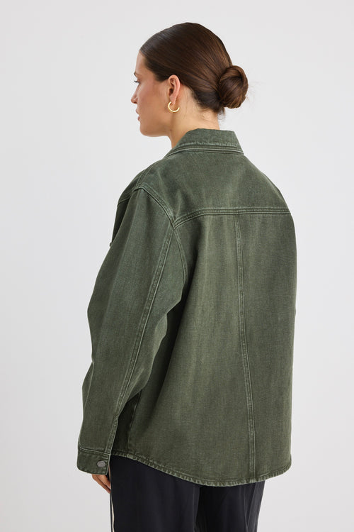 Woman wearing a khaki green washed denim jacket with silver buttons, styled with black pants featuring a cream side stripe.