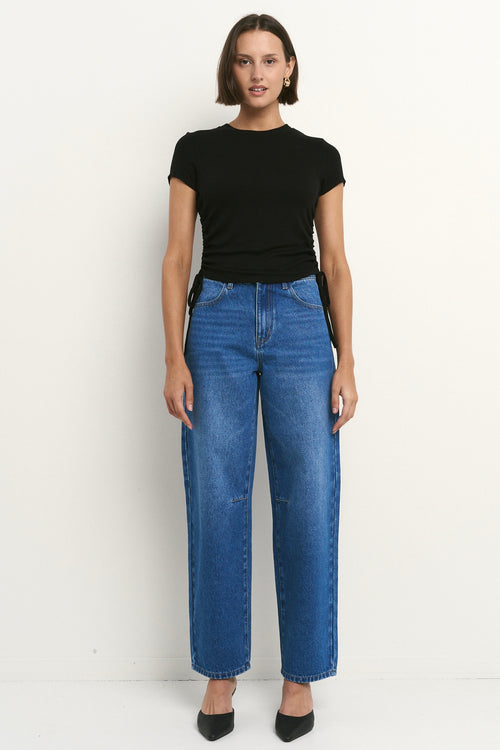 Woman wearing high-rise, blue wide-leg jeans with a black tee and sneakers, styled in a relaxed, casual look.