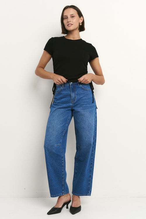 Woman wearing high-rise, blue wide-leg jeans with a black tee and sneakers, styled in a relaxed, casual look.