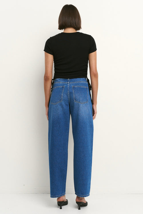 Woman wearing high-rise, blue wide-leg jeans with a black tee and sneakers, styled in a relaxed, casual look.