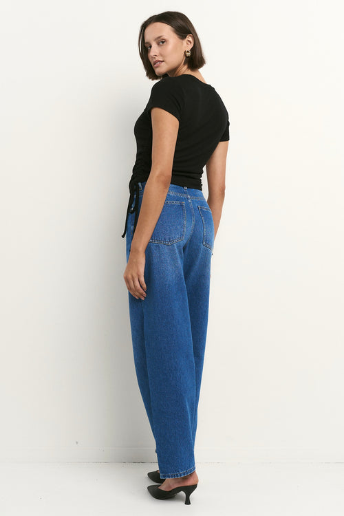 Woman wearing high-rise, blue wide-leg jeans with a black tee and sneakers, styled in a relaxed, casual look.
