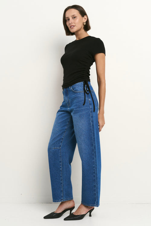 Woman wearing high-rise, blue wide-leg jeans with a black tee and sneakers, styled in a relaxed, casual look.