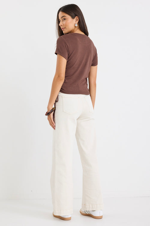 Woman wearing a fitted chocolate brown short sleeve tee with ribbed texture and adjustable side ruching, paired with high-rise cream jeans.
