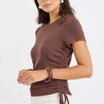 Woman wearing a fitted chocolate brown short sleeve tee with ribbed texture and adjustable side ruching, paired with high-rise cream jeans.